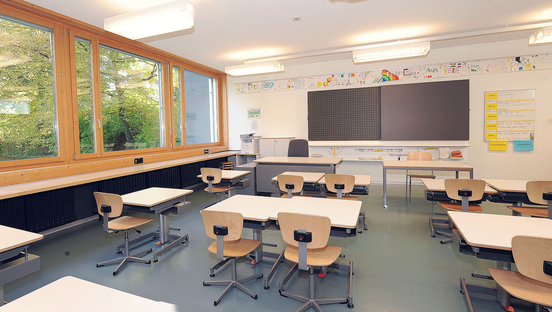 Schulzimmer mit Stühlen, Tischen und Wandtafel.