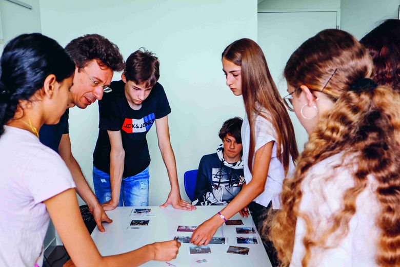 Ein Mann und einige Kinder stehen um einen Tisch. Auf dem Tisch befinden sich Bilder.