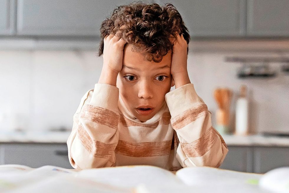 Ein Kind rauft sich die Haare und blickt auf einige offene Bücher, die vor ihm auf einem Tisch liegen.