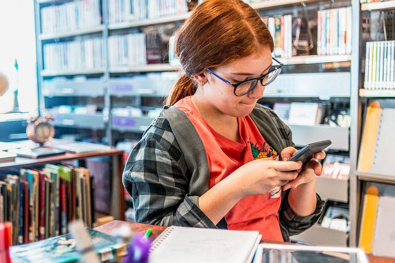 1152467914 Ein Mädchen steht in der Bibliothek und konzentriert sich auf ihr Handy.