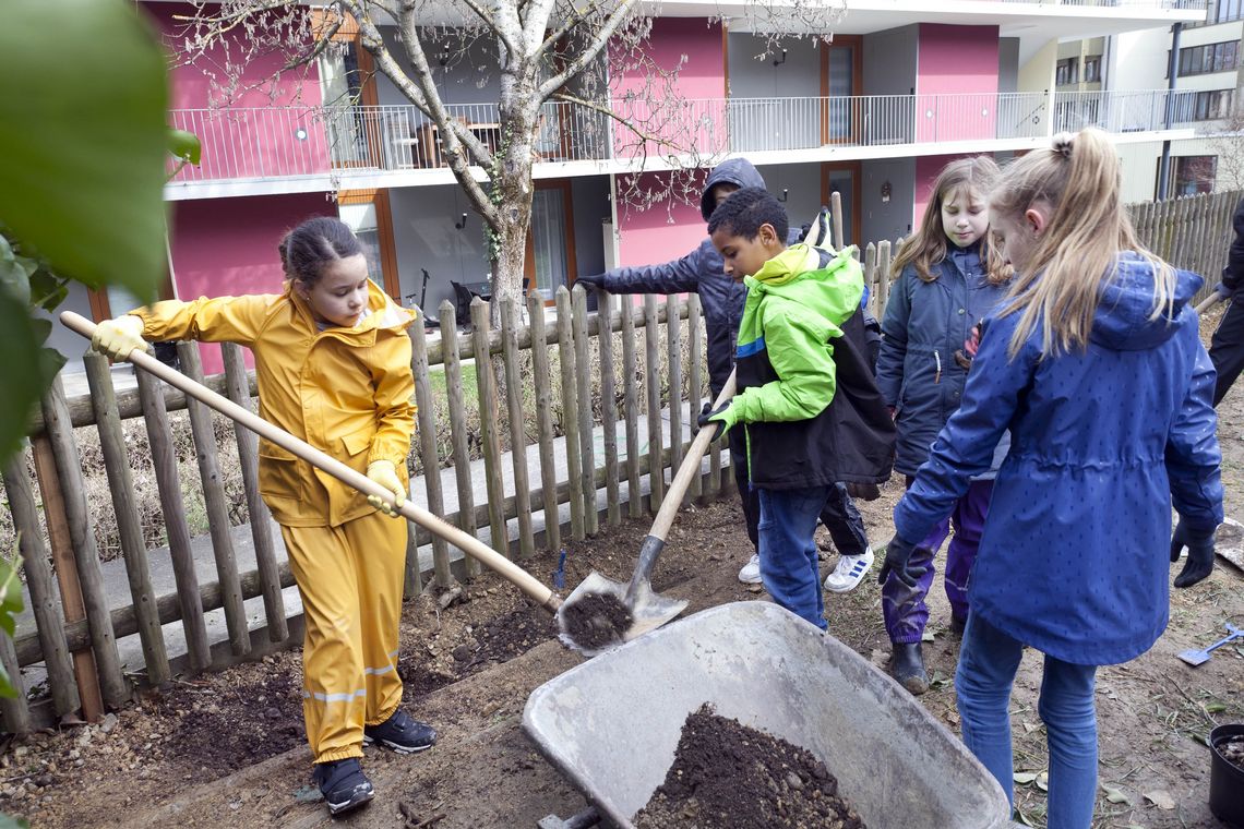 Primarschulkinder füllen eine Karrette mit Erde. 