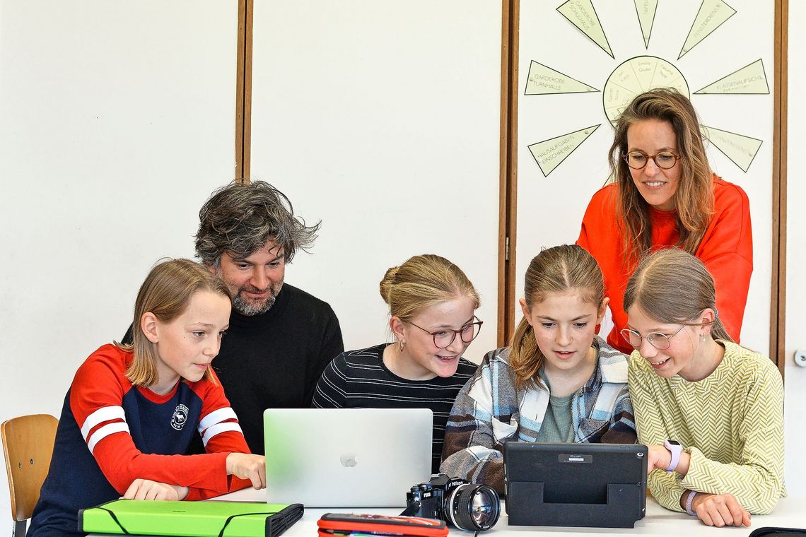Zwei erwachsene Personen und vier Kinder schauen auf zwei Laptops.