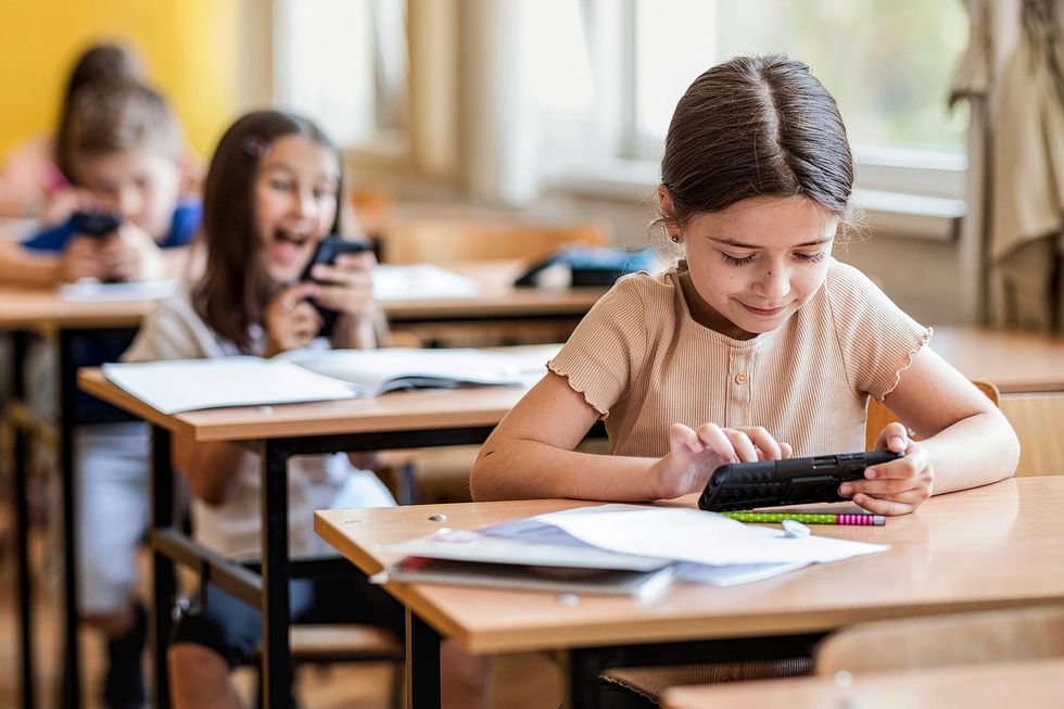 Kinder sitzen an Schulbänken und benutzen ihre Smartphones.