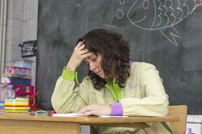 Tired teacher in classroom Lehrerin sitzt am Pult und stützt sich den Kopf.