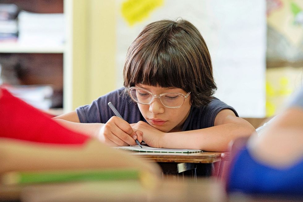 1210376129 Ein Schulkind schreibt konzentriert in sein Heft.