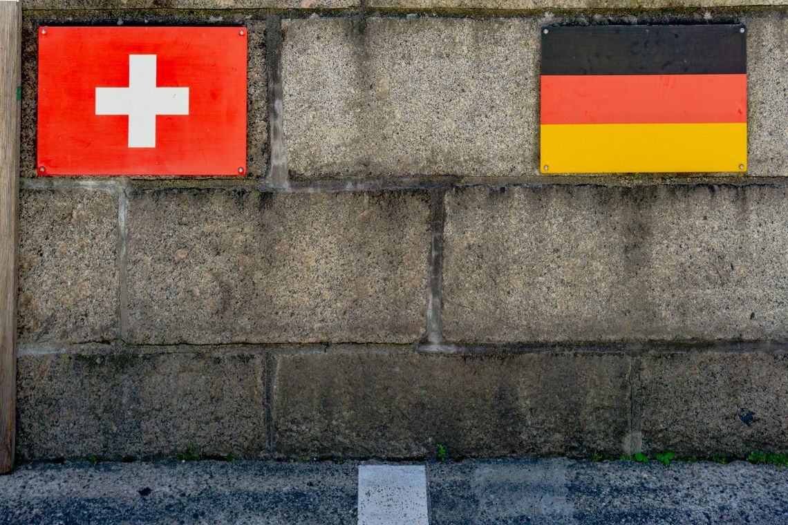 An einer Mauer sind zwei Schilder angebracht. Eines zeigt die Schweizer Flagge, das andere die deutsceh Flagge.