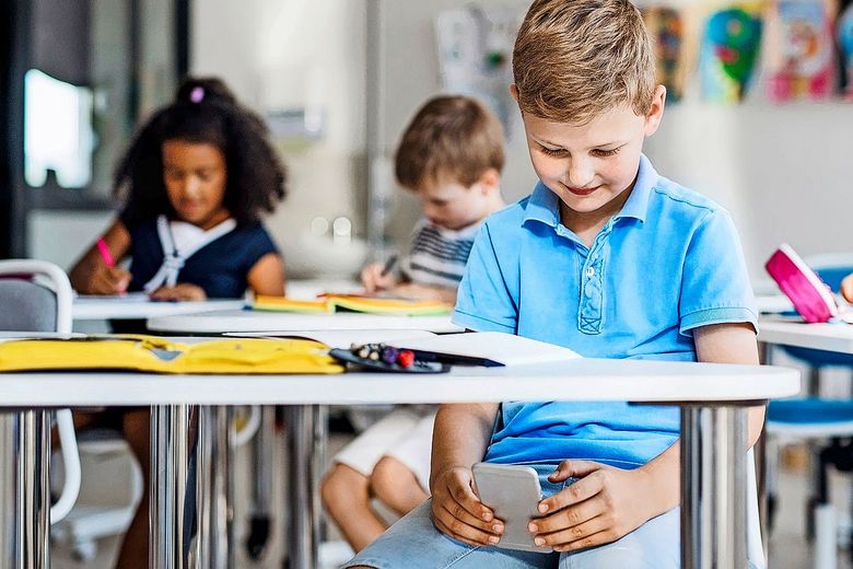 Kind schaut auf sein Smartphone während des Unterrichts.