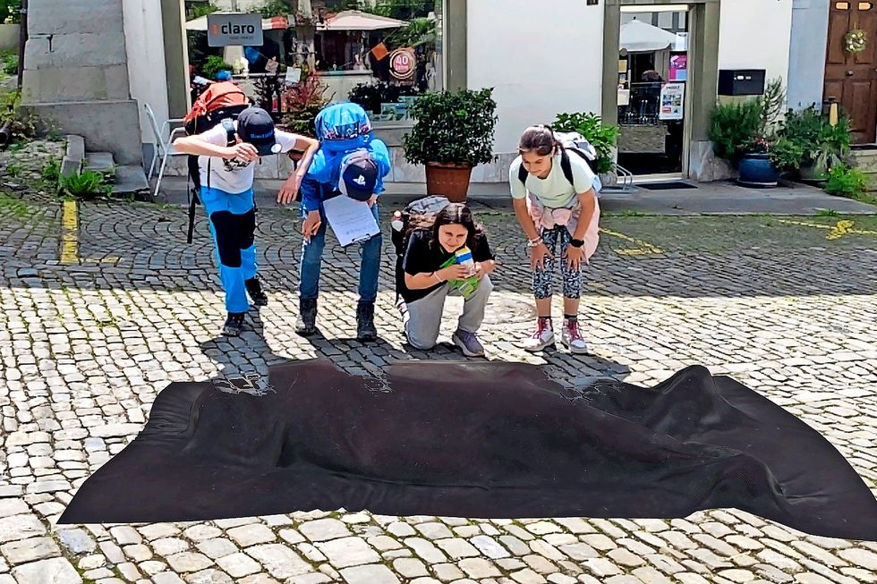 Vier Kinder betrachten einen schwarzen grossen Sack, der auf dem Boden liegt.