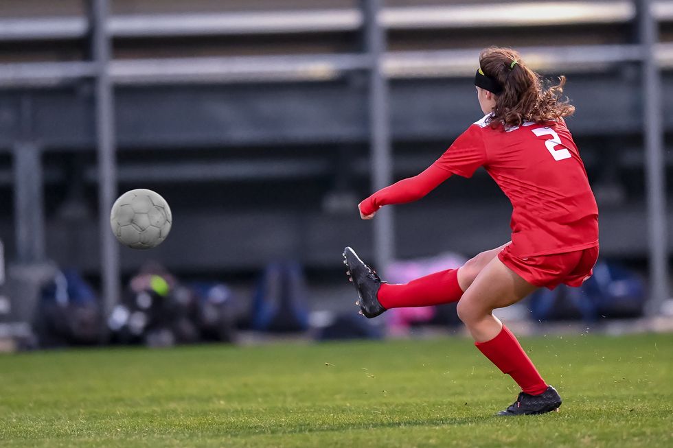 Ein Ball fliegt über den Rasen, weil eine Fussballerin in gekickt hat. 