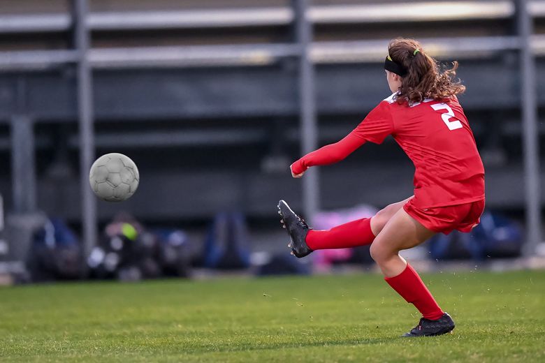 Ein Ball fliegt über den Rasen, weil eine Fussballerin in gekickt hat. 