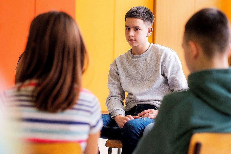 Ein Teenager hört seinen zwei Klassenkameraden zu.