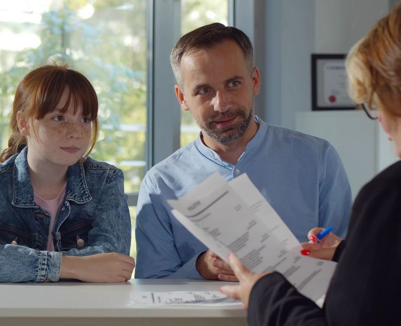 Ein Mädchen und ein Mann sitzen gemeinsam mit einer Frau an einem Tisch.