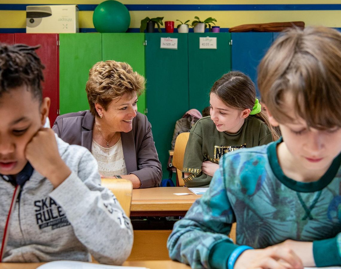 Die Zürcher Bildungsdirektorin Silvia Steiner sitzt während eines Schulbesuchs mit Kindern an einer Schulbank.