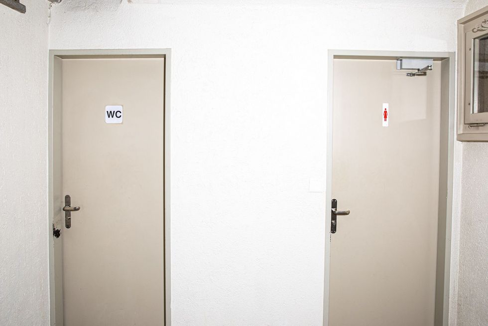 Eine Toilettentür, auf der das klassische Symbol für Frauen abgebildet ist, neben einer Toilettentür, auf der schlicht WC steht.