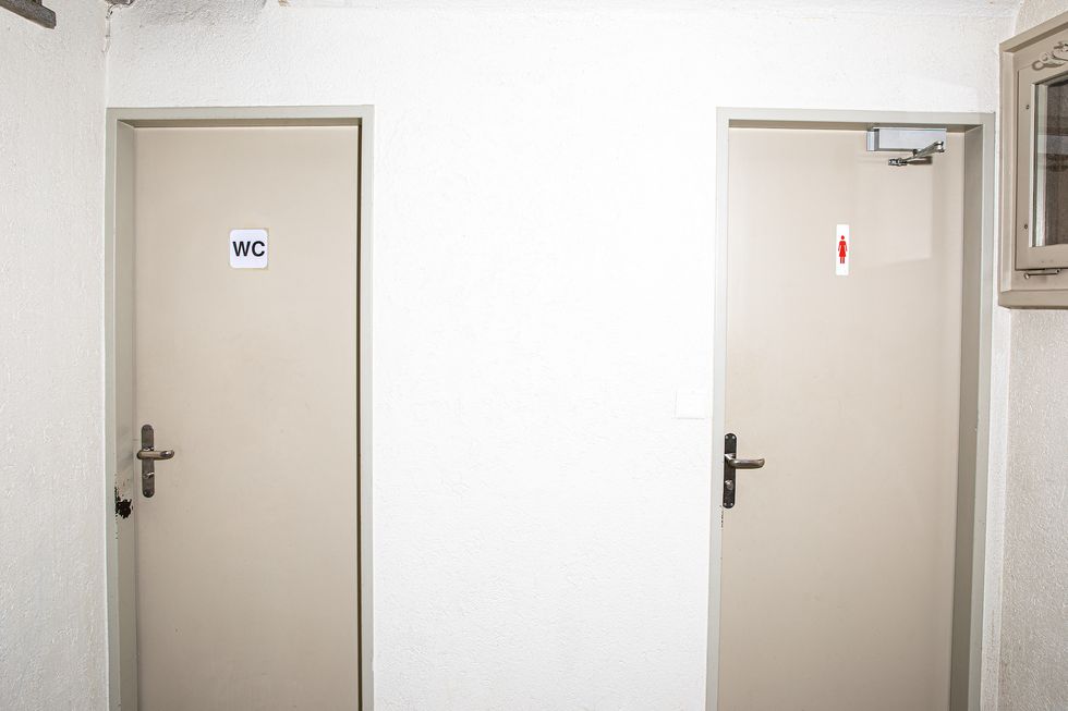 Eine Toilettentür, auf der das klassische Symbol für Frauen abgebildet ist, neben einer Toilettentür, auf der schlicht WC steht.