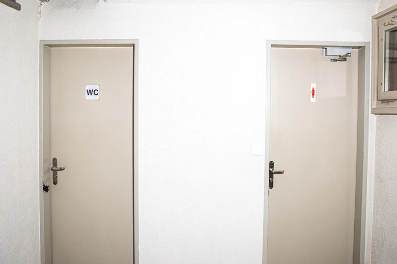 Eine Toilettentür, auf der das klassische Symbol für Frauen abgebildet ist, neben einer Toilettentür, auf der schlicht WC steht.