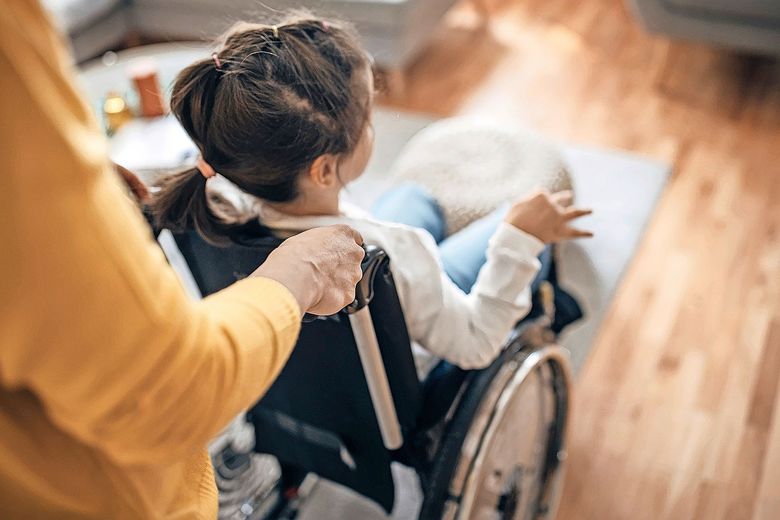 Erwachsene Person schiebt ein Kind im Rollstuhhl