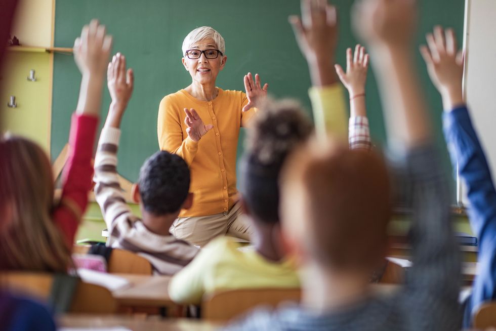 Eine Frau steht vor einigen Kindern, welche je eine Hand in die Luft strecken.