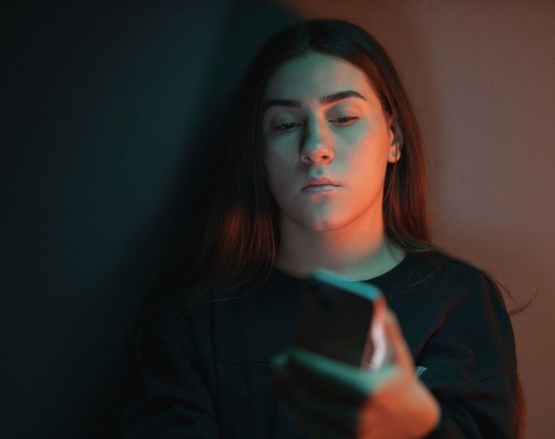 Ein Schatten fällt auf das Gesicht einer Teenagerin, die auf ihr Handy schaut.