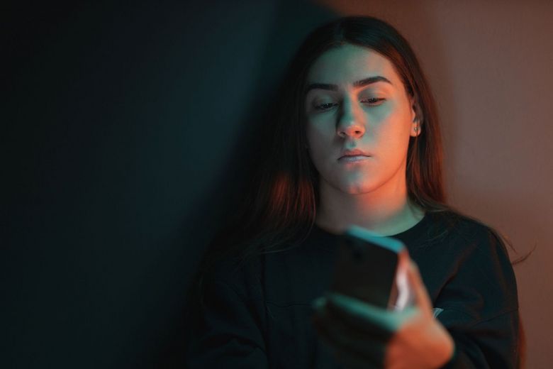 Ein Schatten fällt auf das Gesicht einer Teenagerin, die auf ihr Handy schaut.