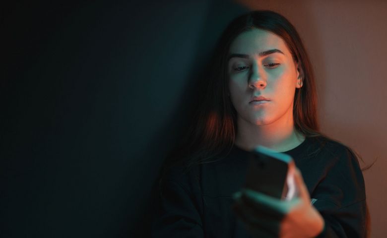 Ein Schatten fällt auf das Gesicht einer Teenagerin, die auf ihr Handy schaut.