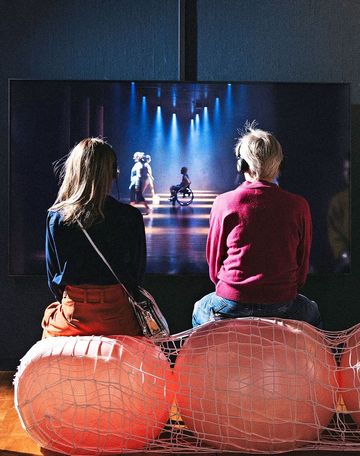 Zwischen den Rücken zweier Mädchen hindurch sieht man einen Rollstuhl auf der Tanzfläche.