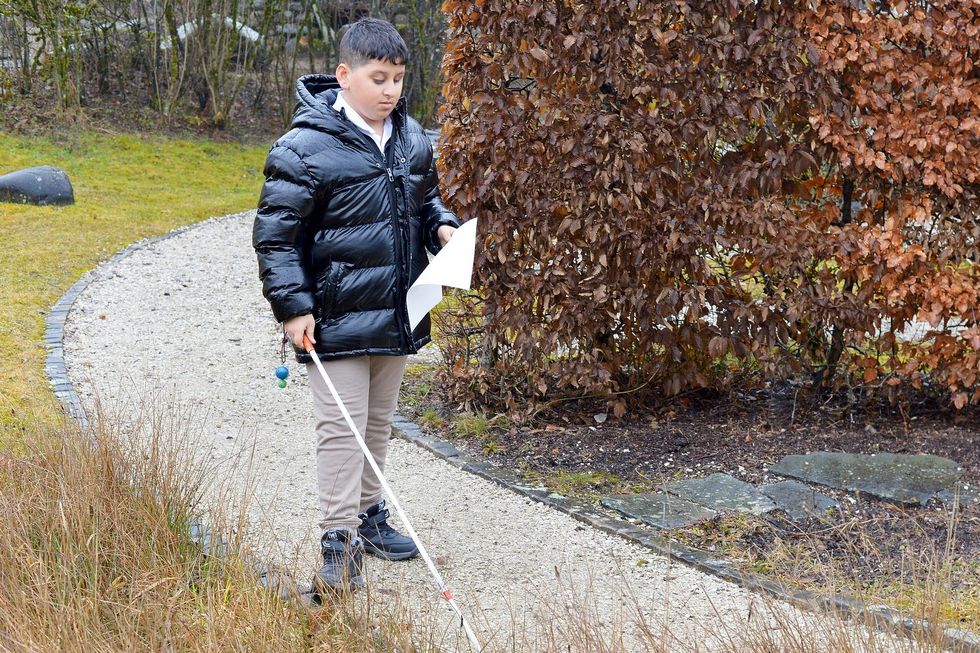 Ein Junge geht mit einem Blindenstock einen Weg entlang.