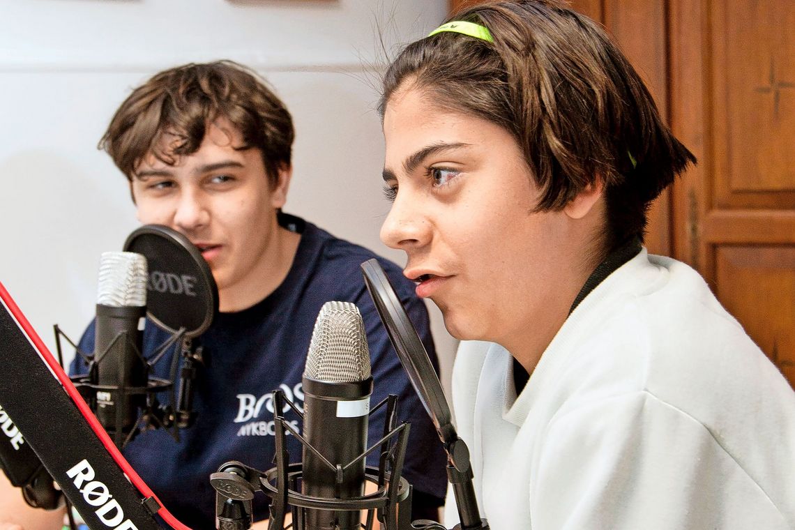 Ein Schüler spricht, beobachtet von einem Kollegen, in ein Mikrofon.
