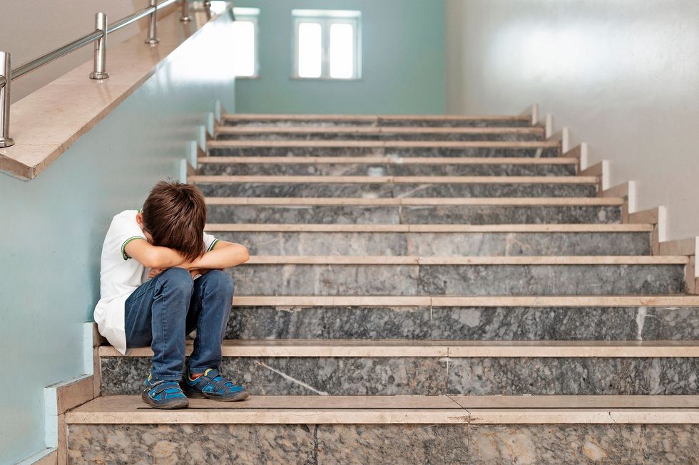 Ein Kind sitzt auf einer Treppe und verbirgt sein Gesicht hinter seinen Knien.