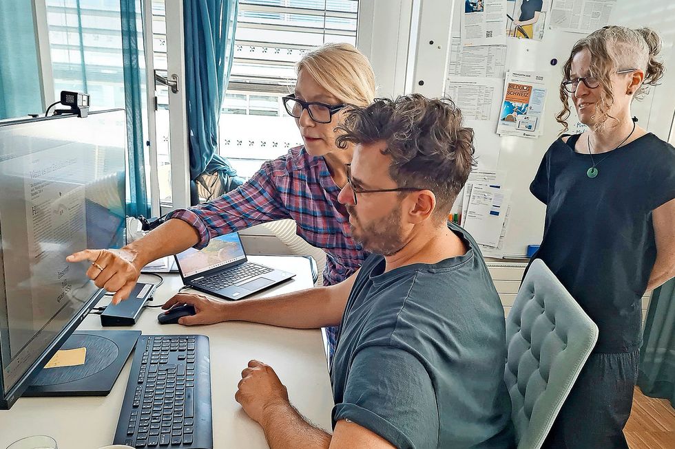 Drei Personen vor einem Bildschirm.