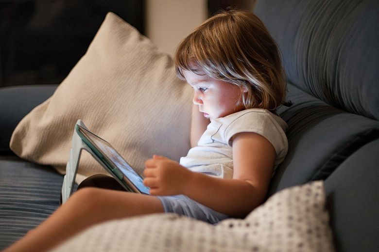 Ein Tablet wirft kaltes Licht auf das Gesicht eine Kindes.