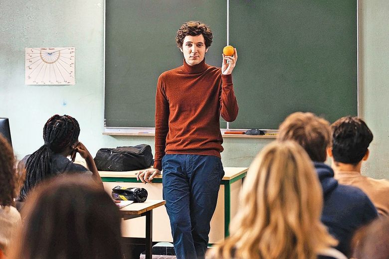 Ein Lehrer steht vor der Klasse und hält eine Orange hoch.