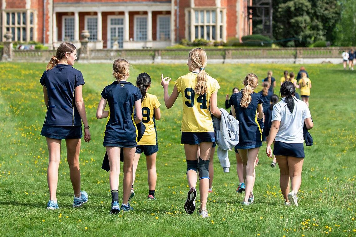 Junge Frauen in einheitlichem Sport-Tenue gehen über den Rasen in Richtung eines herrschaftlichen Hauses.