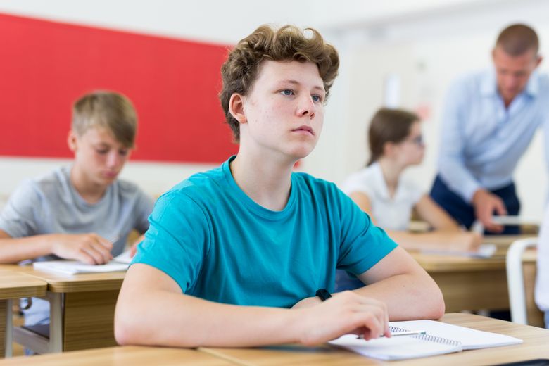 Ein Schüler an einem Pult schaut gedankenverloren vor sich hin.