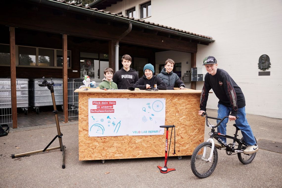 Hinter dem Tresen der mobilen Velowerkstatt steht eine Gruppe von Schülern