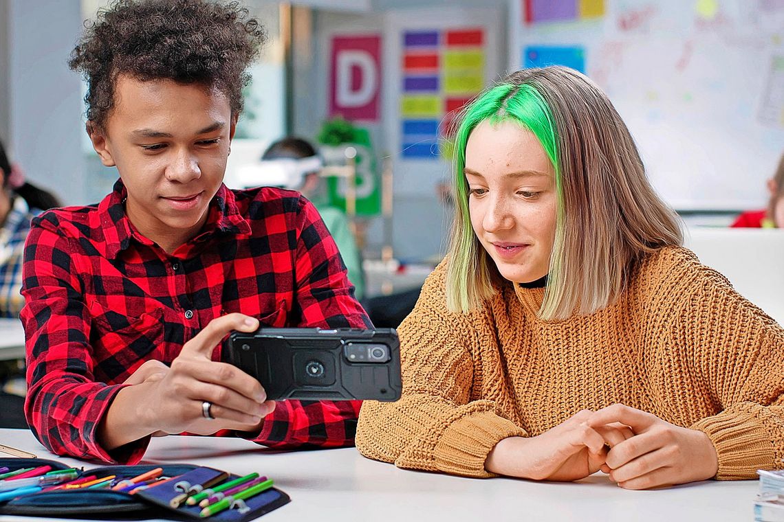 Zwei Teenager sitzen beisammen und starren in ein Handy.