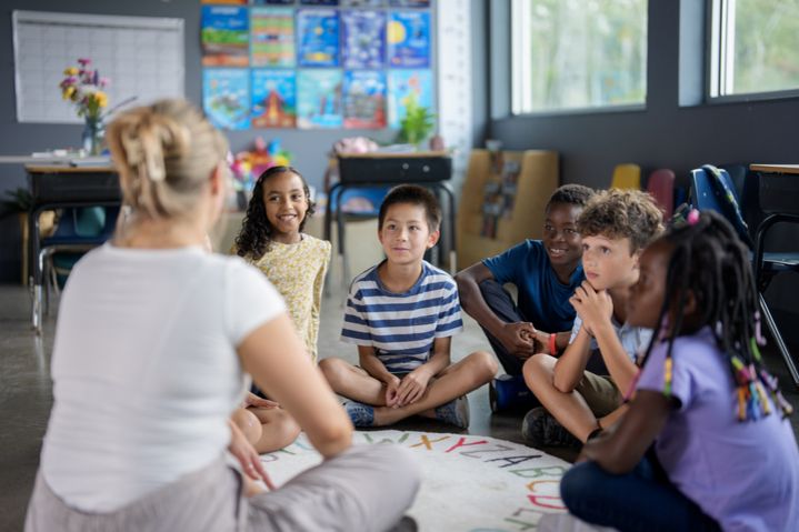 Eine Frau sitzt mit einigen Kindern unterschiedlicher Herkunft zusammen.
