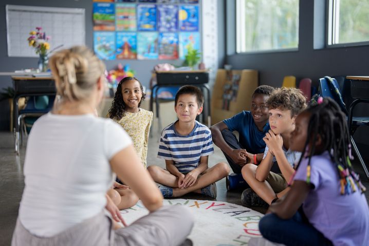 Eine Frau sitzt mit einigen Kindern unterschiedlicher Herkunft zusammen.