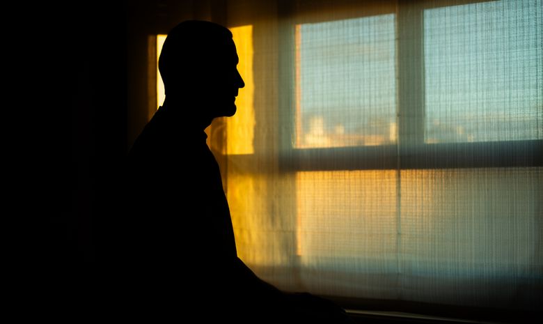 Mann steht im Gegenlicht vor einem Fenster.