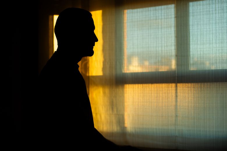 Mann steht im Gegenlicht vor einem Fenster.