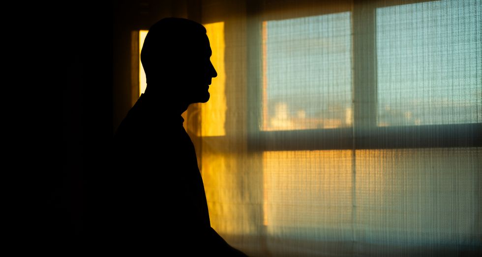 Mann steht im Gegenlicht vor einem Fenster.