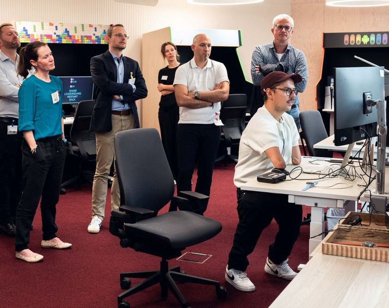 Patrick Schilling steht am Computer umgeben von Arbeitskolleginnen und -kollegen.