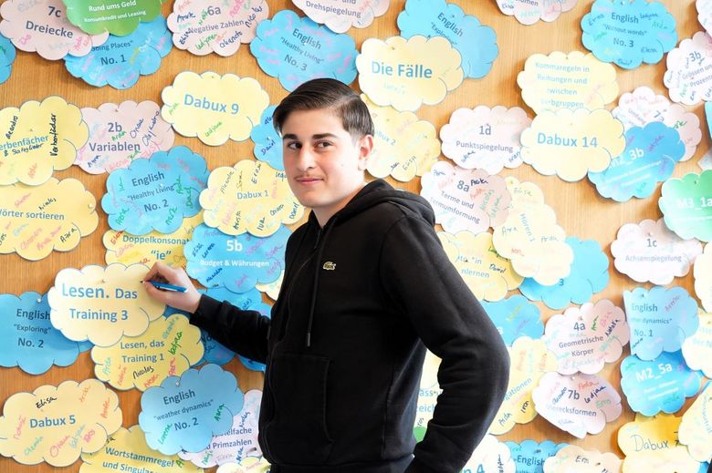 Junge steht vor einer Wand, die mit Wolken aus Papier.