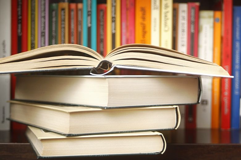 Ein aufgeschlagenes Buch liegt auf einem Bücherstapel im Buchregal.