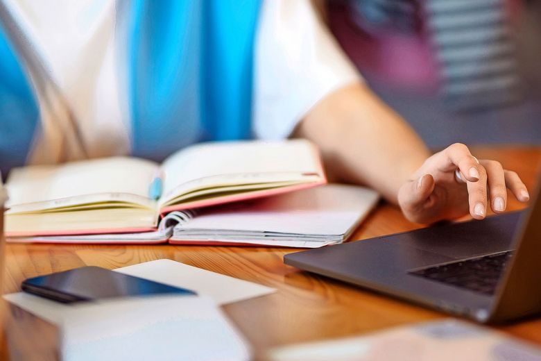 Eine Person hat zwei offene Bücher vor sich auf dem Tisch liegen und bedient einen Laptop.