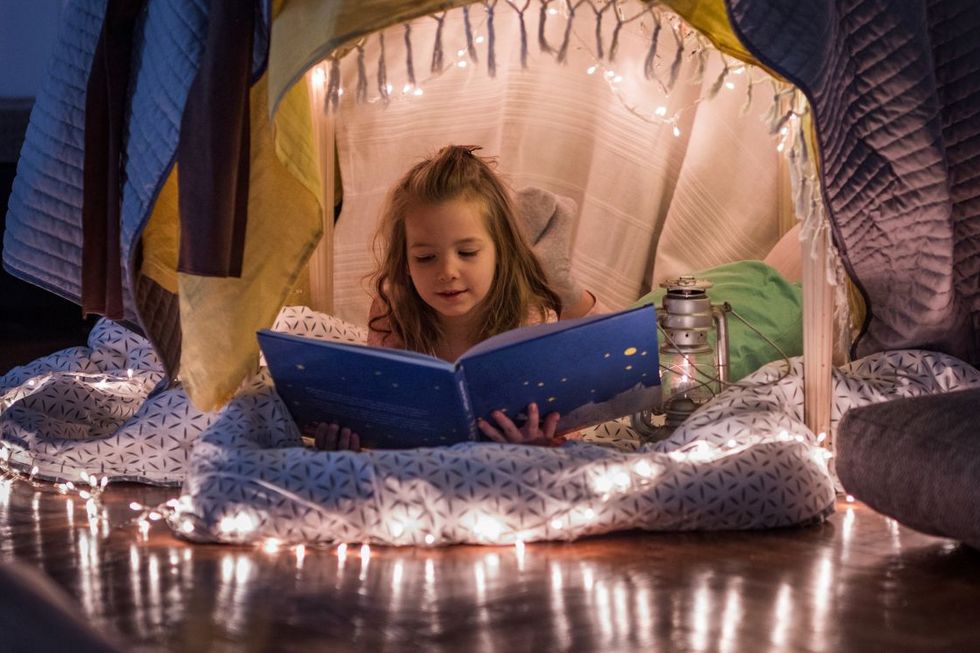 Ein Mädchen liegt in Höhle aus Tüchern und liest in einem grossen Buch.
