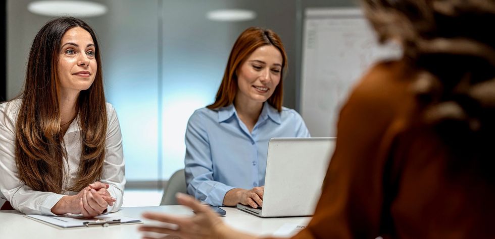Zwei Frauen sitzen einer dritten Person am Tisch gegenüber.