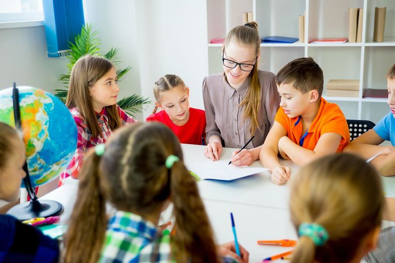 Eine Lehrerin und eine Gruppe Kinder arbeiten zusammen an einem Aufgabenblatt.