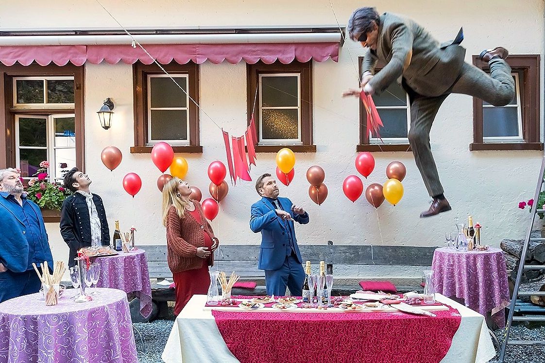 Ein verkleideter Mann fällt aus mehreren Metern höhe auf einen gedeckten Tisch.