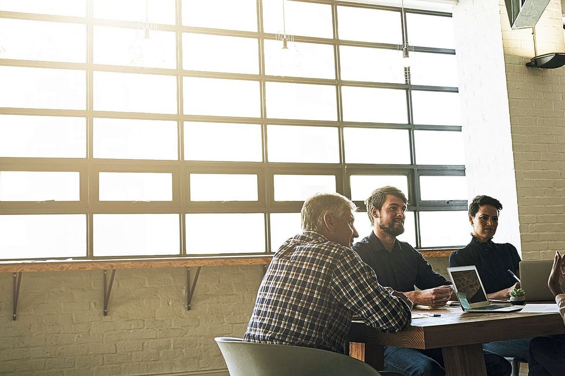 Vier Leute sitzen um einen Tisch und haben Laptops vor sich. Im Hintergrund scheint die Sonne durch ein Fenster.